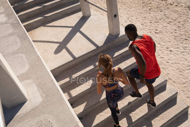 Vue en angle élevé de jeunes couples multiethniques courant des escaliers près de la plage — Photo de stock