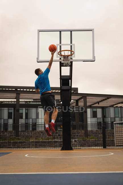 Rückansicht eines Basketballspielers, der einen Korb auf einem Basketballfeld gegen ein Gebäude im Hintergrund schießt — Stockfoto