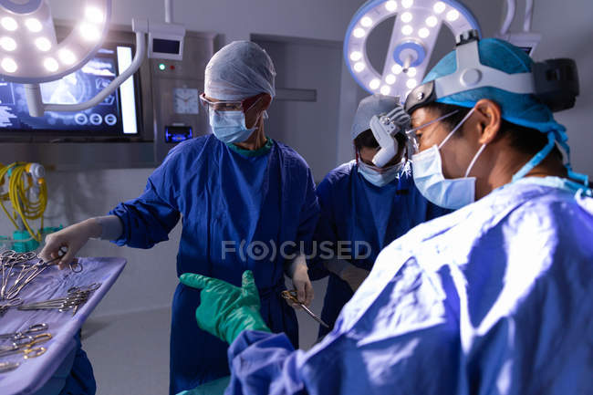 Вид збоку хірургів зосереджена в операційний зал під час операції, хоча вони вибирають інструменти в лікарні — стокове фото