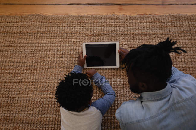 High angle view of African-American father and son using digital tablet while lying on carpet at home — Stock Photo