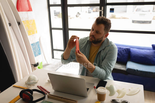 Vista frontal do homem caucasiano examinando a barbatana de prancha em uma oficina — Fotografia de Stock