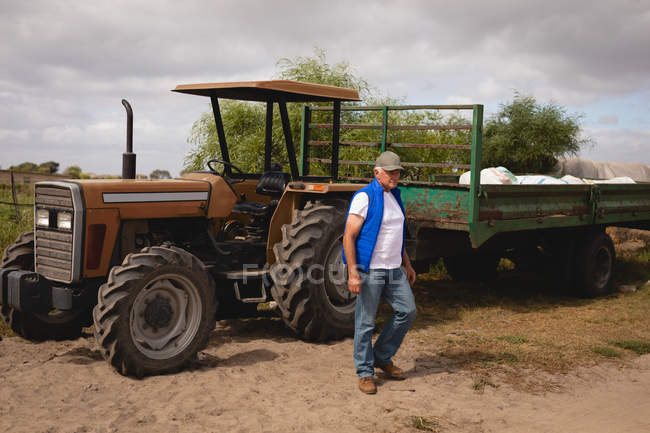 Vista lateral de um agricultor masculino caucasiano sênior saindo do trator na fazenda em um dia ensolarado — Fotografia de Stock