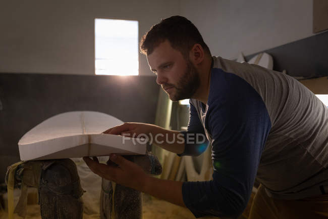 Seitenansicht eines kaukasischen Mannes, der mit seinen Händen fühlt, wenn das Surfbrett in einer Werkstatt glatt ist — Stockfoto