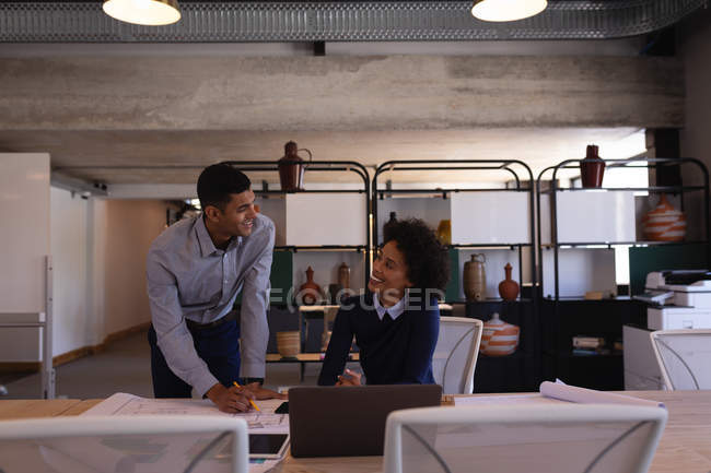 Вид спереду щасливих молодих бізнесменів змішаної раси, які обговорюють синій друк в офісі — стокове фото