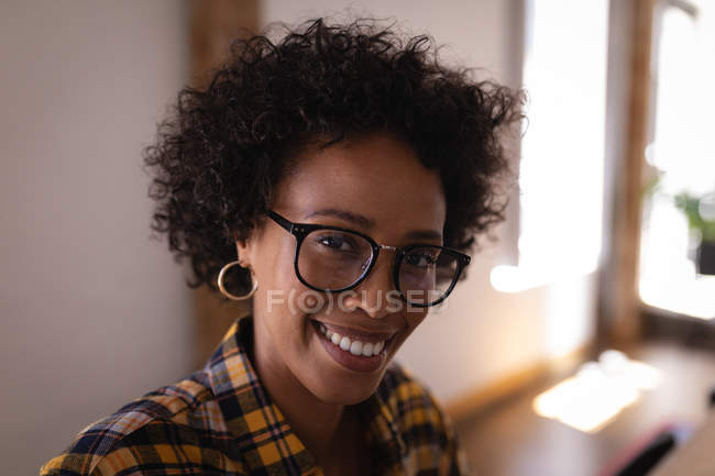 Портрет красивой бизнесвумен смешанной расы, сидящей в современном офисе. Она смотрит и улыбается на камеру — стоковое фото