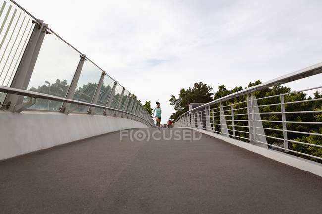 Vista frontal de la joven mujer de raza mixta corriendo por una pasarela en la ciudad - foto de stock