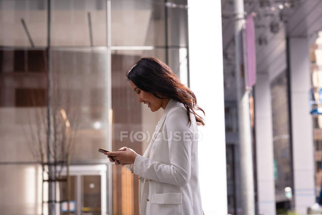Vue latérale de la femme asiatique utilisant un téléphone portable tout en se tenant dans un couloir en verre — Photo de stock