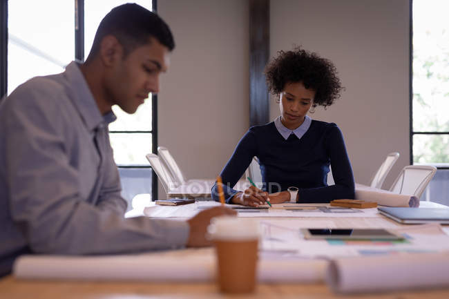 Vista frontal de jóvenes empresarios de raza mixta enfocados que trabajan en planes con lápices en una sala de reuniones - foto de stock