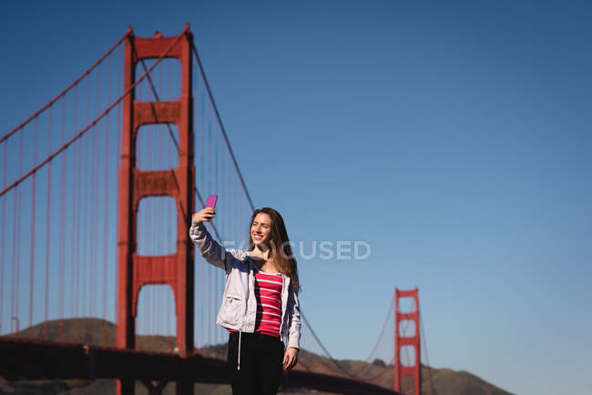 Vue à angle bas de la belle femme prenant selfie près du pont suspendu — Photo de stock