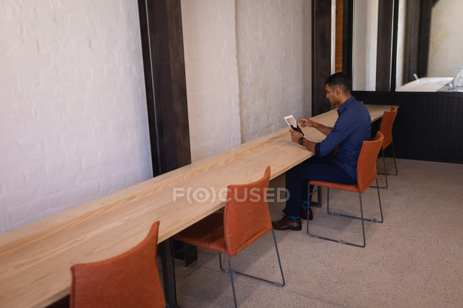 Вид ззаду молодого бізнесмена змішаної раси, що використовує цифровий планшет за столом в сучасному офісі — стокове фото