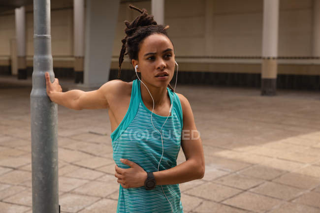 Vista frontale della giovane donna di razza mista che ascolta musica sugli auricolari mentre si esercita in città — Foto stock