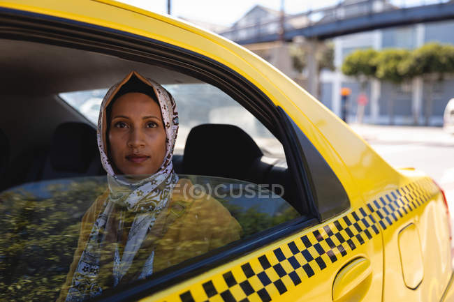 Front view of thoughtful mixed race woman looking at the camera while sitting in taxi on a sunny day — Stock Photo