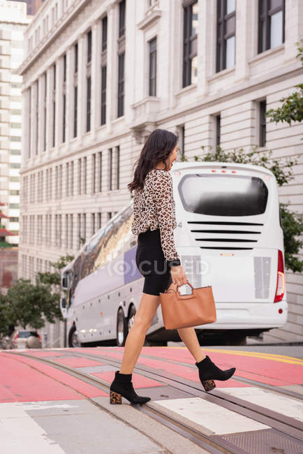 Side view of Asian woman talking on mobile phone while crossing the street — Stock Photo