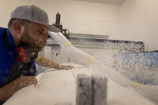 Side view of Caucasian man blowing on surfboard residue in workshop — Stock Photo