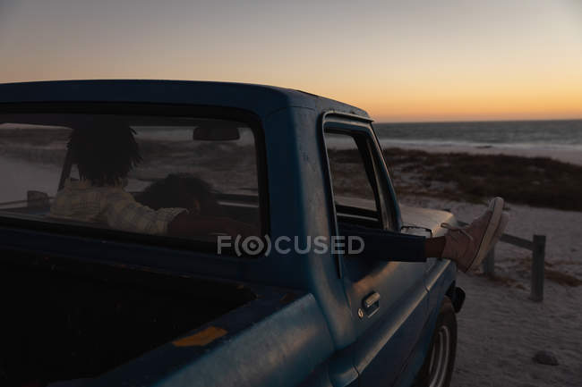 Rückansicht eines romantischen Paares, das sich im Auto am Strand bei Sonnenuntergang entspannt — Stockfoto