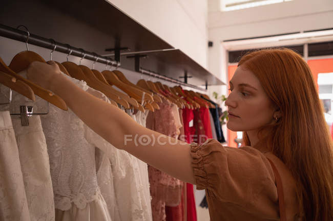 Vista laterale della bella giovane donna caucasica che sceglie il vestito in boutique — Foto stock