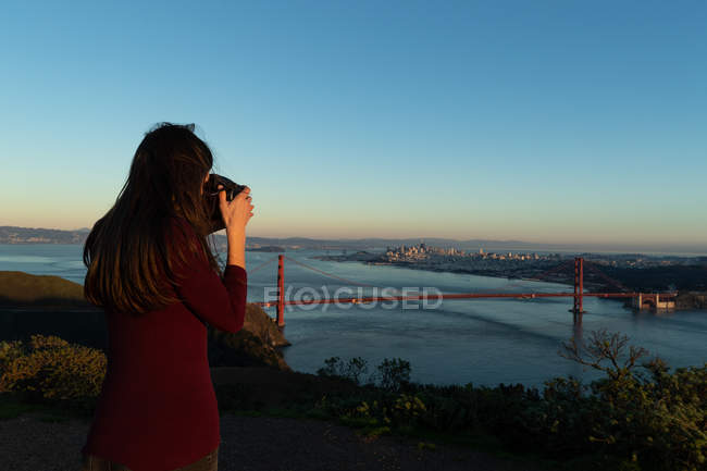 Rear view of woman taking a picture of a bridge on a sunny day — Stock Photo
