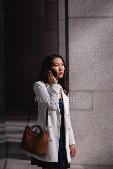 Seitenansicht einer asiatischen Frau, die auf dem Flur mit dem Handy telefoniert — Stockfoto