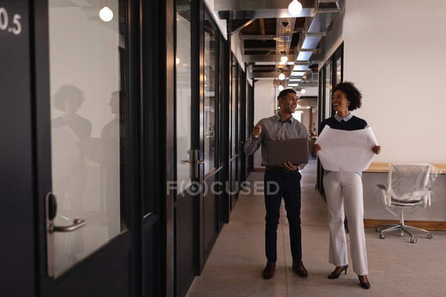 Frontansicht glücklicher junger Geschäftsleute mit gemischter Rasse, die im Amt miteinander interagieren, während sie eine Blaupause in der Hand halten — Stockfoto