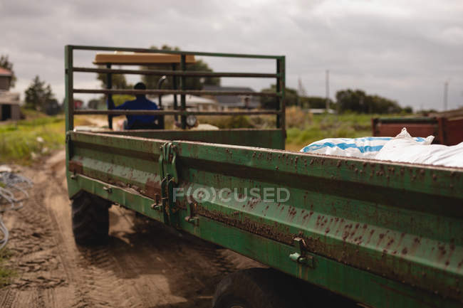 Rear view of African American male farmer driving tractor with loaded trailer on farm — Stock Photo