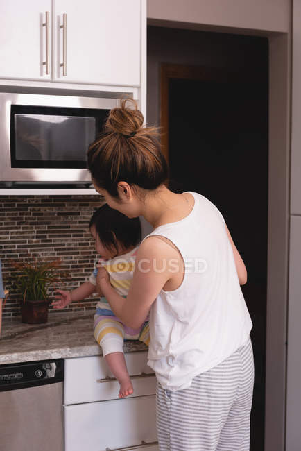 Visão traseira da mãe e da filha asiáticas olhando para a planta da panela na cozinha em casa — Fotografia de Stock