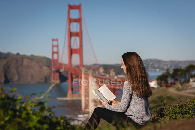 Вид сбоку красивой женщины, читающей книгу, сидя на склоне горы — стоковое фото