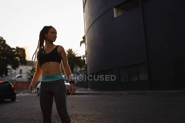 Vue de face de la jeune femme de race mixte se reposant après l'exercice dans la ville — Photo de stock