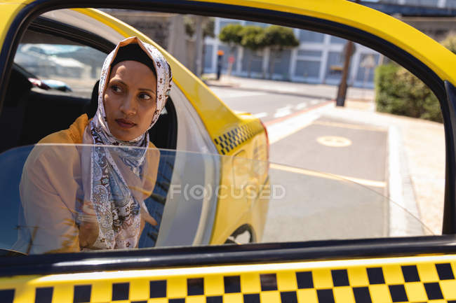 Vista frontal de la estresada mujer de raza mixta que sale del taxi en un día soleado - foto de stock