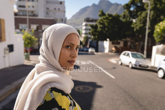 Vue latérale d'une belle jeune femme métissée en hijab traversant la rue par une journée ensoleillée — Photo de stock