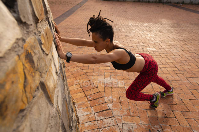 Vue latérale de la forme jeune femme de race mixte faisant de l'exercice dans la ville — Photo de stock
