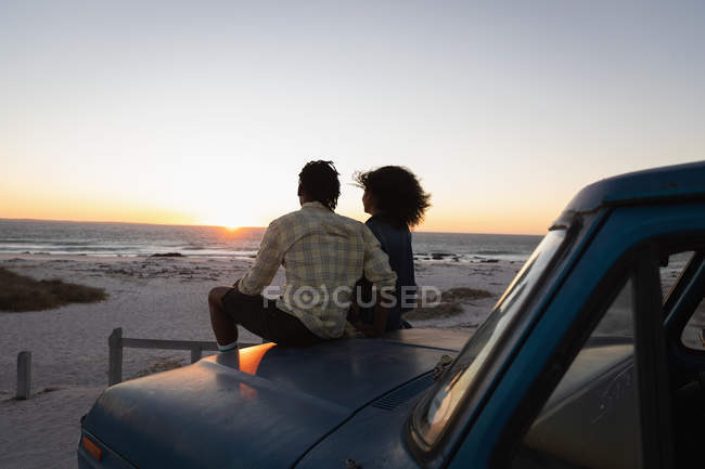 Vista traseira do casal romântico sentado em um carro na praia durante o pôr do sol — Fotografia de Stock