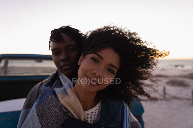 Vista frontal do casal romântico afro-americano apoiando-se no carro na praia ao pôr do sol — Fotografia de Stock