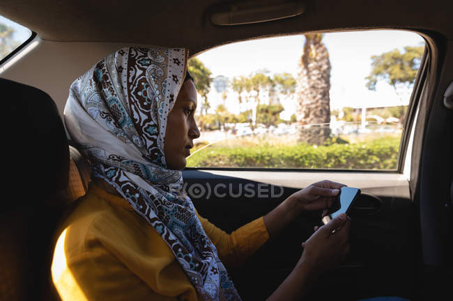 Вид збоку красива змішана жінка, що використовує мобільний телефон під час подорожі в машині — стокове фото