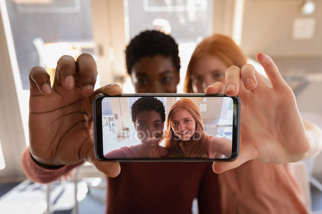 Frontansicht junger Freundinnen gemischter Rassen, die in einem Café ein Selfie mit dem Handy machen — Stockfoto