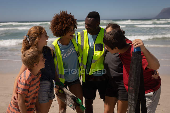 Vista frontal del grupo de voluntarios multiétnicos de pie juntos en la playa en un día soleado - foto de stock