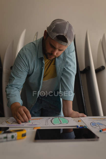 Vista frontal del hombre caucásico concentrado haciendo bosquejo de tabla de surf en un taller - foto de stock