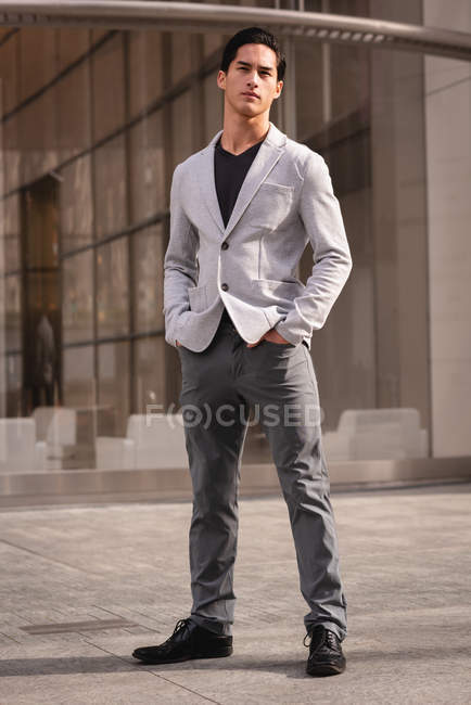 Vista frontal do homem asiático bonito pensativo que está perto do pavimento do edifício — Fotografia de Stock