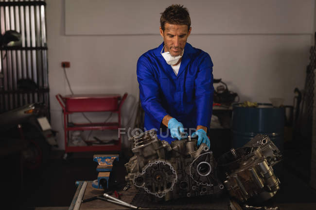 Вид спереди на молодого кавказского мотомеханика, ремонтирующего велосипедный двигатель в гараже — стоковое фото