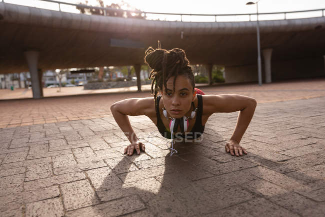 Vista frontale della vestibilità giovane donna di razza mista che fa esercizio push-up in città — Foto stock
