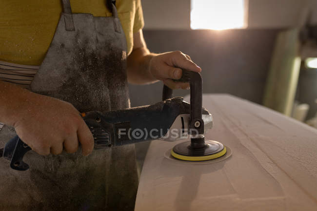 Mid section of man grinding surfboard in a workshop — Stock Photo