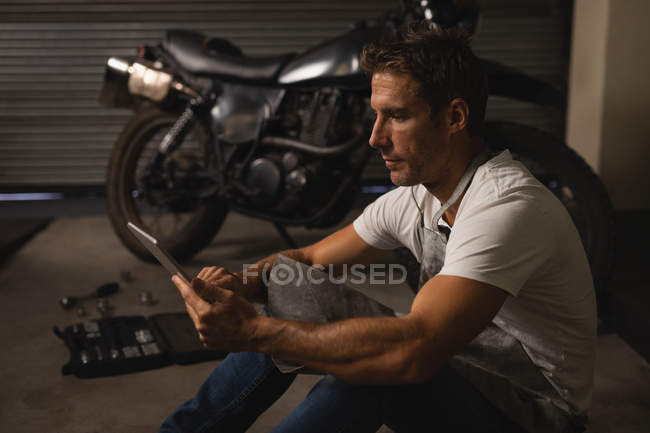 Vista lateral do mecânico de bicicletas masculino caucasiano usando tablet digital na garagem — Fotografia de Stock