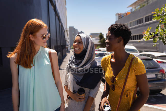 Front view of young mixed race female friends interacting with each other in the city street on sunny day — Stock Photo