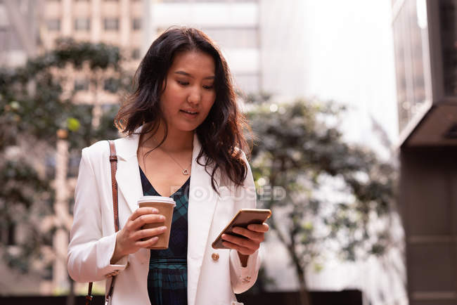 Vista frontal da mulher asiática usando telefone celular enquanto está na rua — Fotografia de Stock