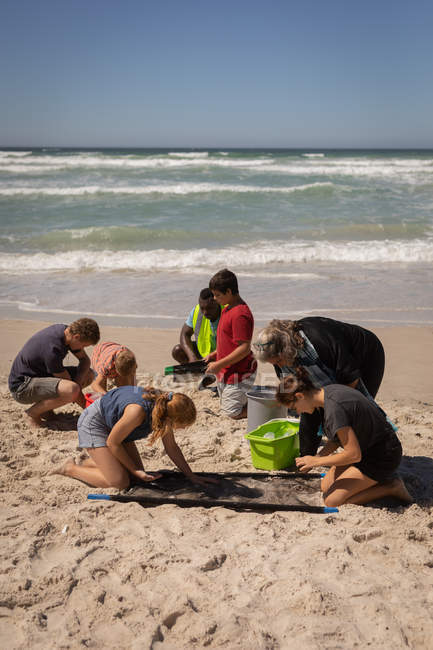Вид на группу мультиэтнических волонтеров, которые в солнечный день находят отходы с помощью специального оборудования на пляже — стоковое фото