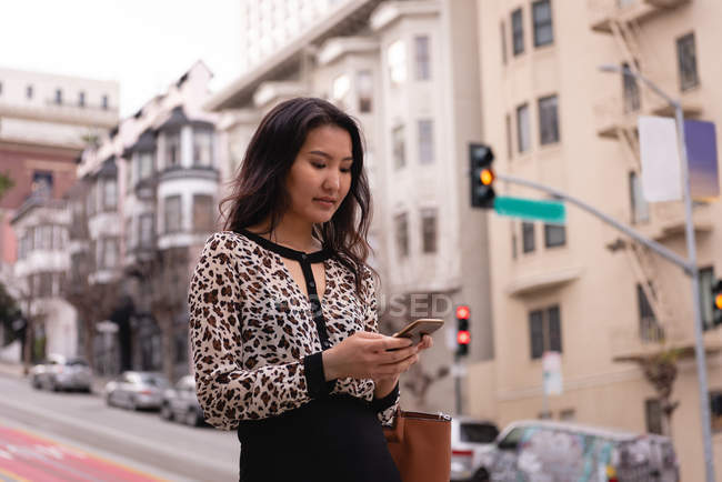 Вид збоку азіатської жінки за допомогою мобільного телефону, стоячи на вулиці — стокове фото