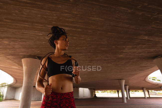 Vista frontal da jovem mulher de raça mista segurando uma corda pulando sob ponte na cidade — Fotografia de Stock