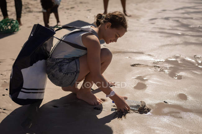 Vista lateral de la joven mujer caucásica voluntaria limpieza playa en un día soleado - foto de stock