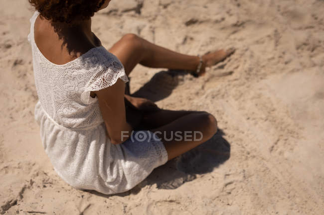 Vue en angle élevé de femme mixte assise sur le sable tout en se relaxant à la plage sur un ensoleillé — Photo de stock