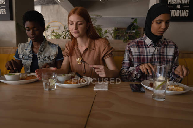 Vista frontale di giovani amiche di razza mista che fanno colazione nel ristorante — Foto stock