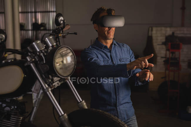 Vista frontal de la mecánica de bicicleta masculina caucásica con auriculares de realidad virtual en el garaje - foto de stock